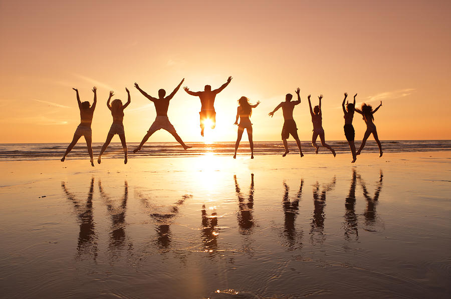 Group of young adults jumping on beach at sunset Photograph by Peter Cade