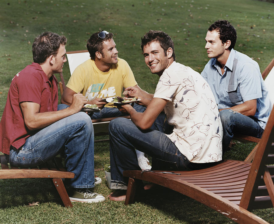 Group of Young Men Sitting on Sun Loungers Eating Photograph by Digital Vision.