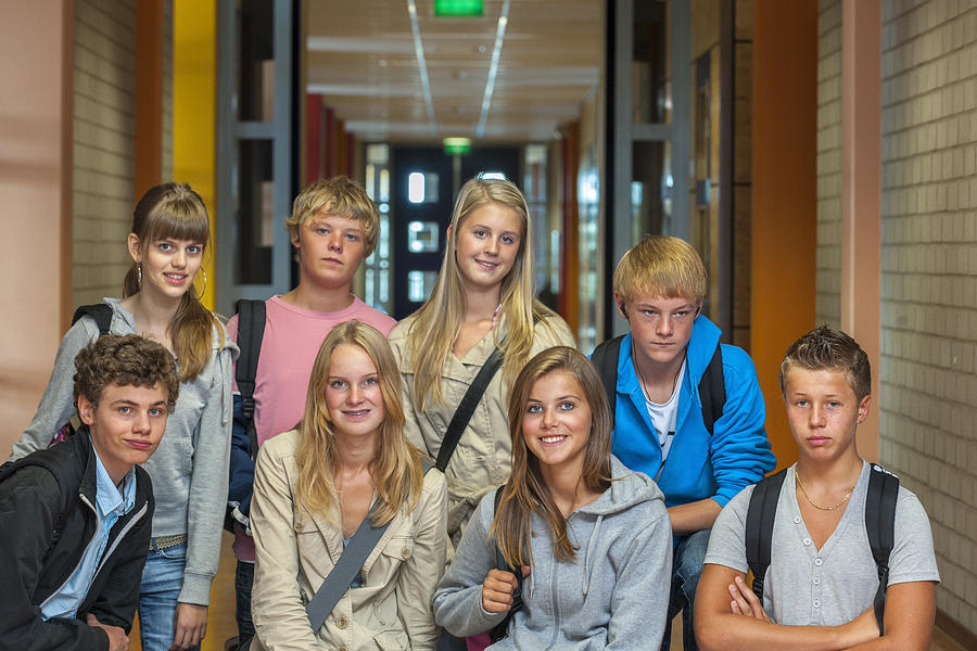 Group shot: three quarter length shot of eight teenage boys and girls with shoulder bags in high school hallway looking at the camera, focus on the girls in the front Photograph by Pidjoe