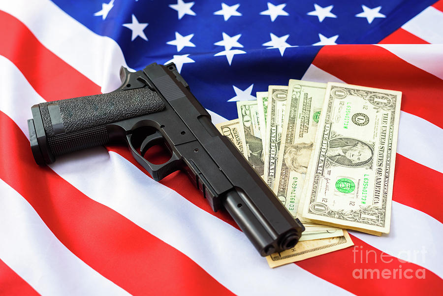 Gun over American flag with dollar bills around it. Photograph by Joaquin Corbalan