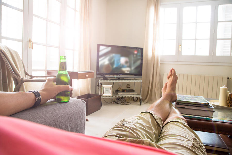 Guy in first person view on sofa with TV and beer. Photograph by Artur Debat
