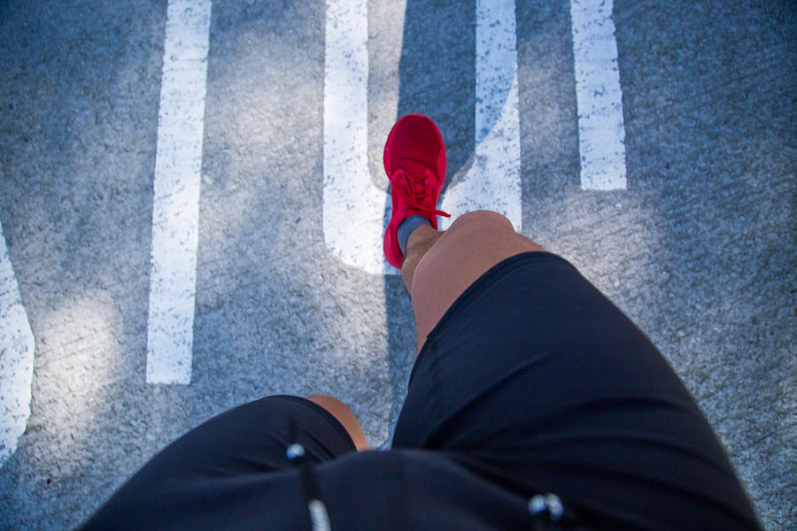 Guy running doing healthy outdoor sport routine in the city, taken the picture from personal perspective looking down with legs, red shoes, and ground. Photograph by Artur Debat