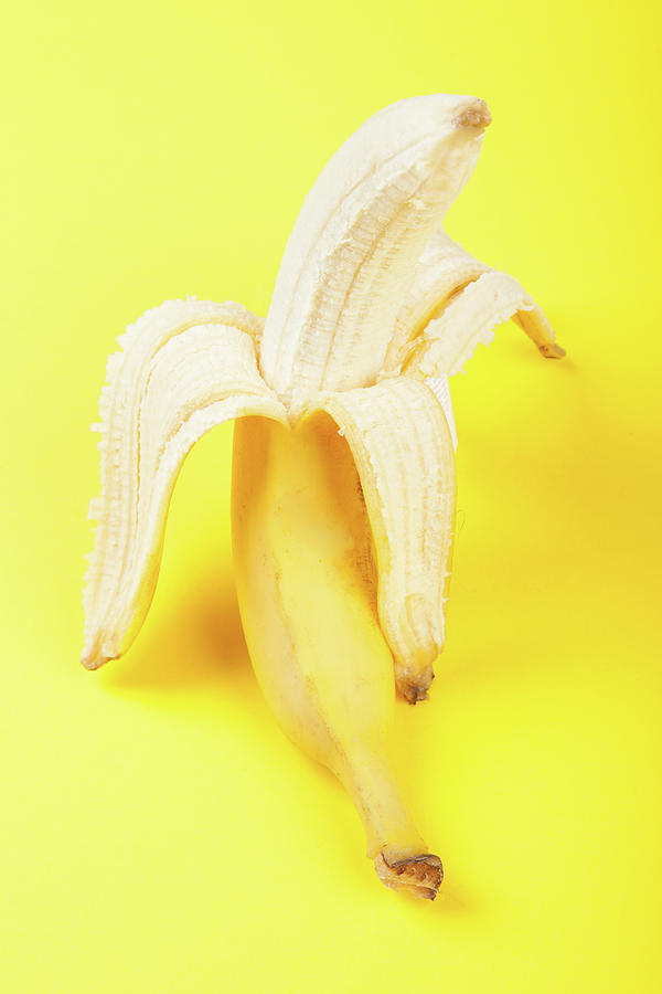 Half Peeled Banana On Yellow Background Photograph