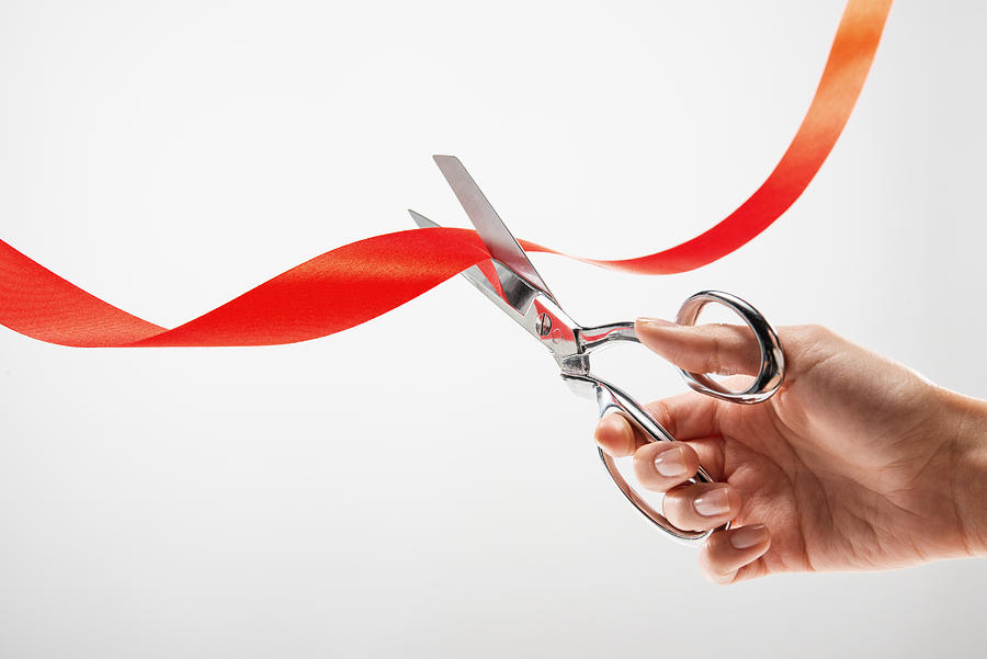 Hand cutting red ribbon with scissors Photograph by PM Images