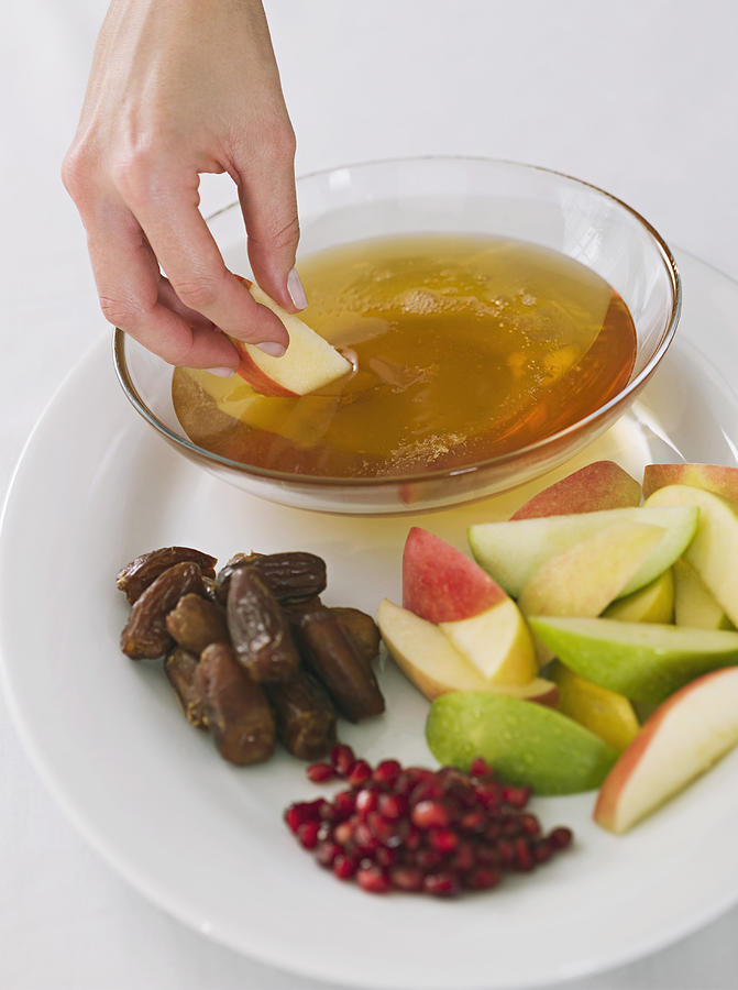 Hand dipping apple into honey with Rosh Hashanah fruit plate Photograph by Jupiterimages