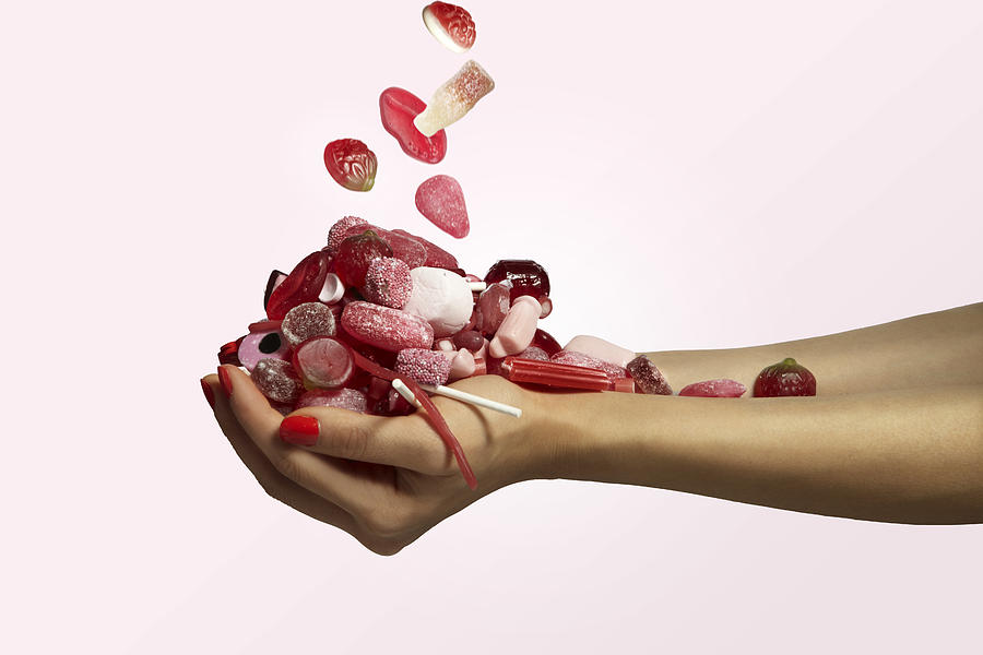 Hand Holding A Bunch Of Red Candy Falling Photograph by Paper Boat Creative