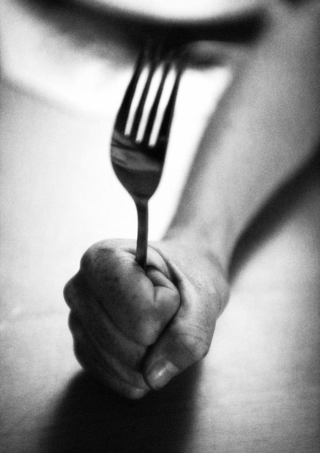 Hand holding fork, close-up, b&w Photograph by Laurent Hamels