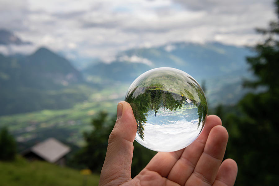 Hand holding glass sphere in front of valley in the alps Photograph by ...