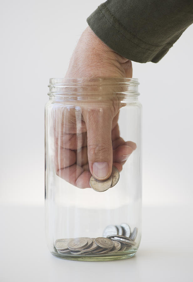 Hand inserting coin into jar Photograph by Tetra Images