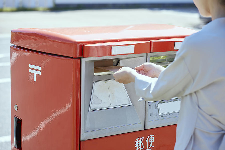 Hand of a young woman putting an envelope in a post box Photograph by West