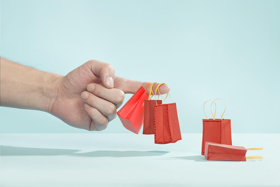 Hand picking up tiny shopping bags on finger Photograph by Paper Boat Creative