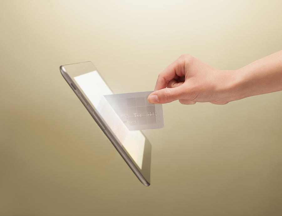 Hand placing credit card into tablet Photograph by PM Images