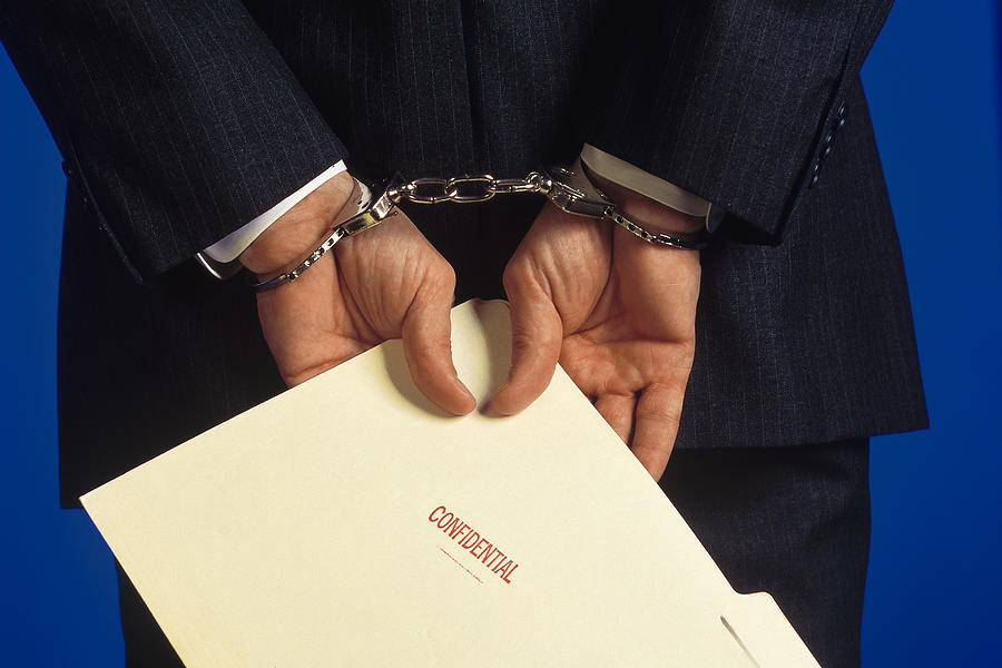 Handcuffed businessman holding folder marked confidential Photograph by Comstock