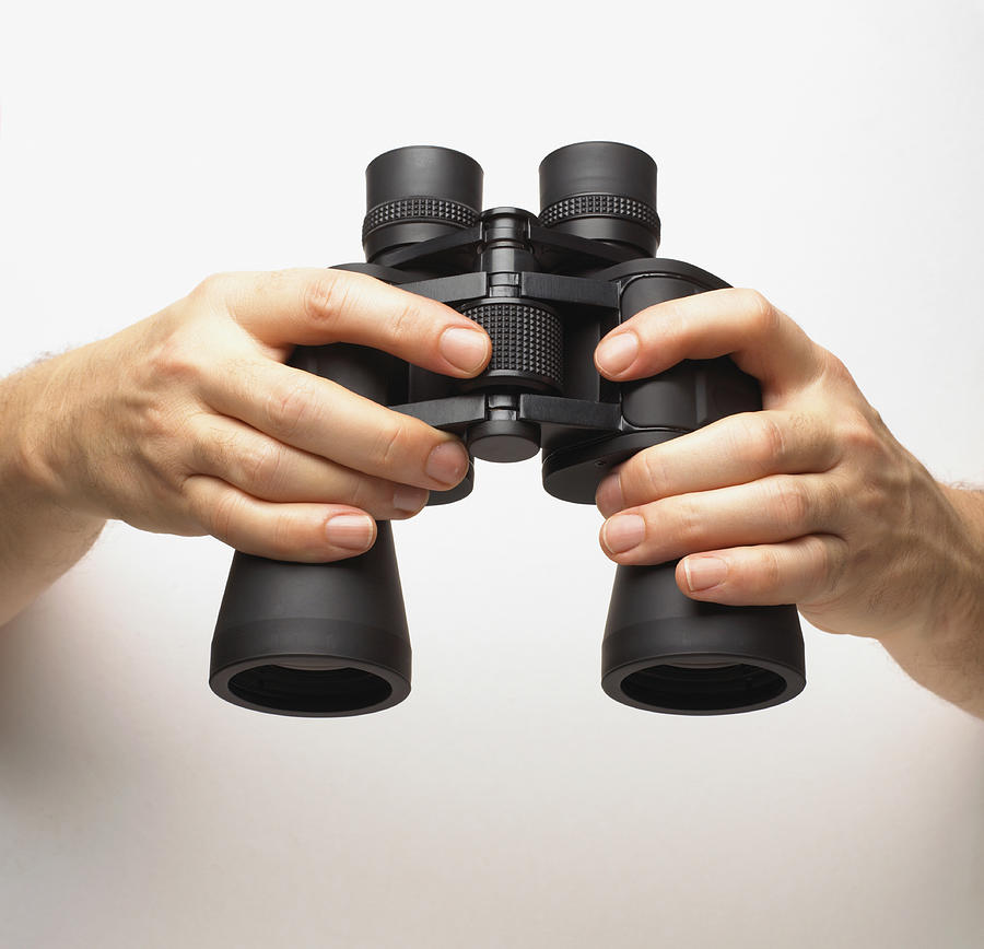 Hands holding binoculars, finger turning central knob, adjusting focus Photograph by Dorling Kindersley