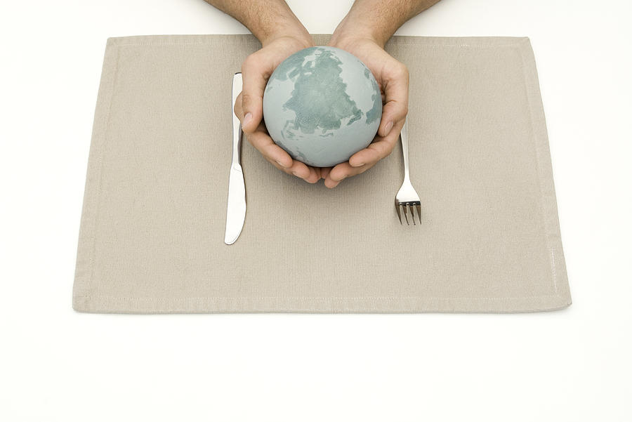 Hands holding globe over placemat and silverware Photograph by PhotoAlto/Michele Constantini