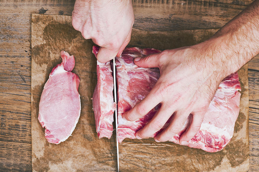 Hands of man cutting raw meat on butcher paper with knife Photograph by Denis Tevekov