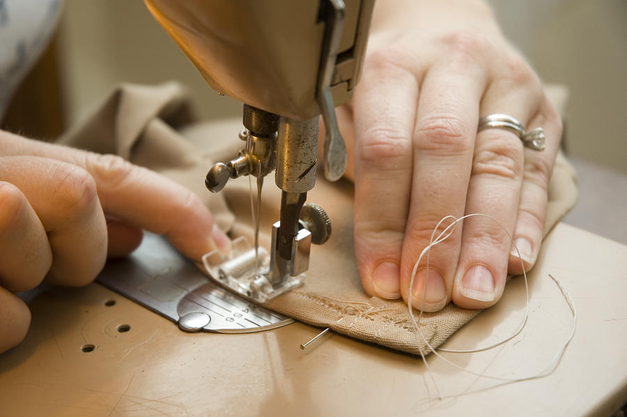 Hands using a sewing machine to sew brown material Photograph by Westhoff