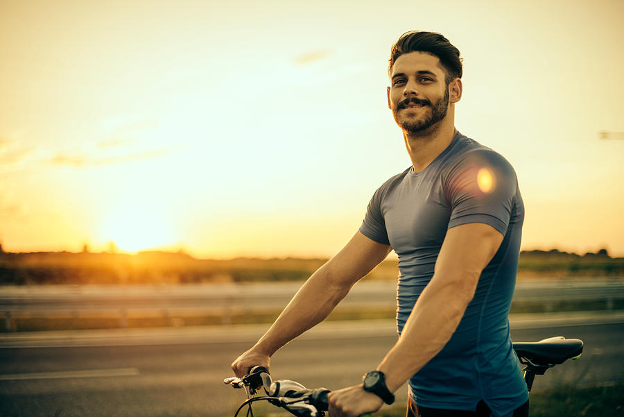 Handsome guy riding mountain bike in sunset Photograph by Drazen_