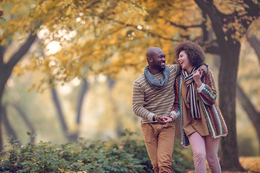 Happy African American couple walking in autumn park and laughing. Photograph by Skynesher