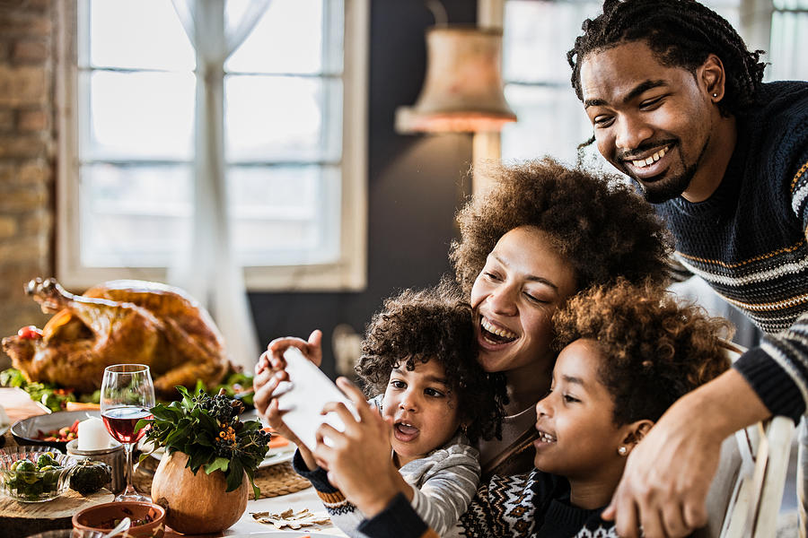 Happy African American family taking a selfie during Thanksgiving lunch. Photograph by Skynesher