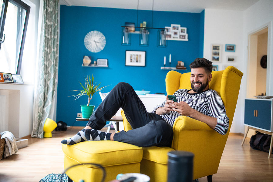 Happy bearded man sitting on armchair and using smart phone Photograph by Miodrag Ignjatovic