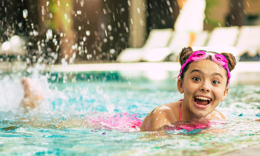 Happy beautiful little smiling girl in goggles and swimsuit in the pool has fun while vacationing or swimming lessons. Photograph by Povozniuk