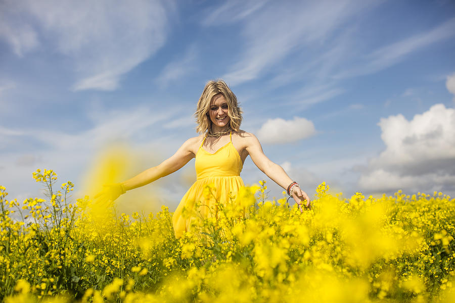 Happy blond woman wearing yellow dress standing in rape field Photograph by Westend61