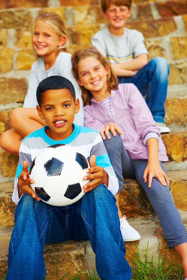 Happy boy holding football and sitting with his friends Photograph by GlobalStock