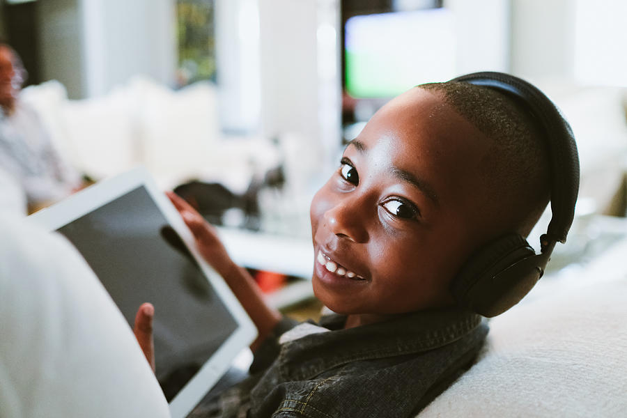 Happy boy taking a break watching a portable tablet with earphones Photograph by Hello Africa