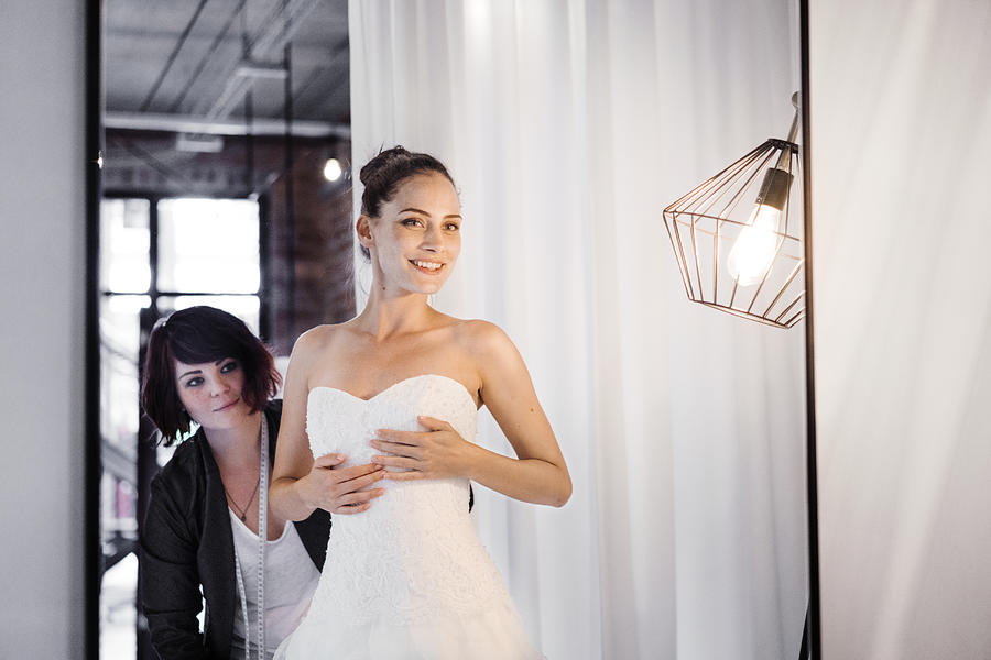 Happy bride wearing gown with tailor working Photograph by Portra