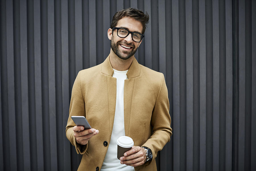 Happy businessman with smart phone and cup in city Photograph by Morsa Images