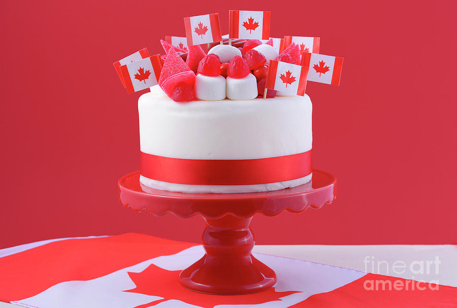 Happy canada day celebration cake with flags, marshmallow and candy  decorations on a red cake stand on a white table against | CanStock
