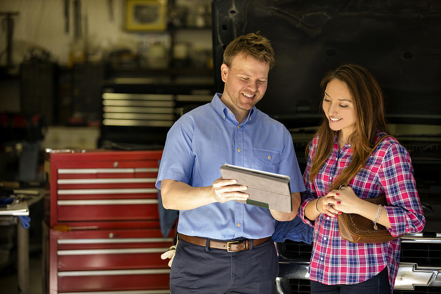 Happy customer discusses repairs with auto mechanic. Digital tablet. Photograph by Fstop123