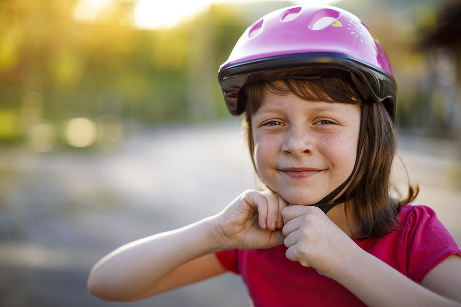 Happy cute girl putting cycle helmet on Photograph by Damircudic