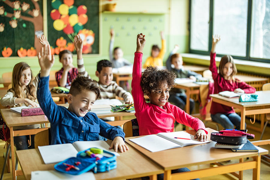 Happy elementary students raising their hands on a class at school. Photograph by Skynesher