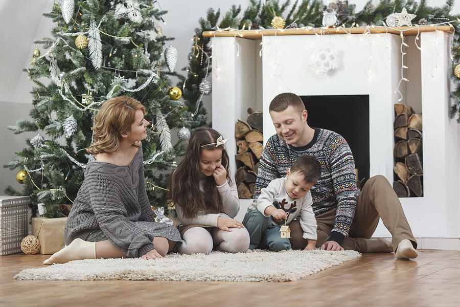 Happy family sitting on rug by Christmas tree at home Photograph by Vasily Pindyurin