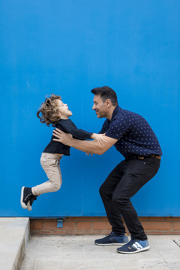 Happy father playing with son at blue wall Photograph by Westend61