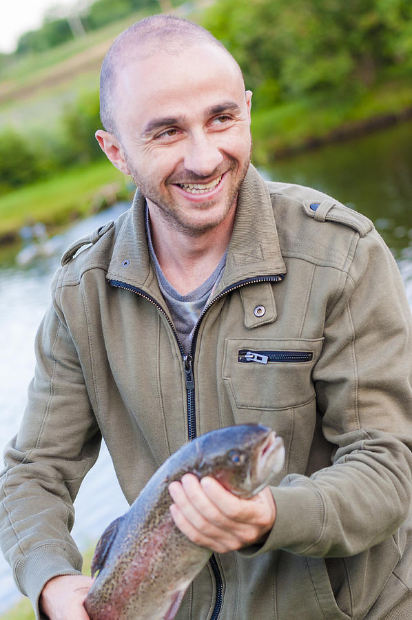 Happy fishing man smiling holding caught Trout fish in hands Photograph by Ykd