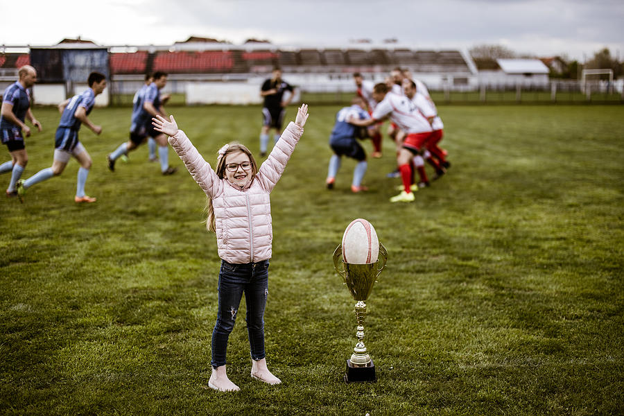 Happy girl cheering during rugby match on playing field. Photograph by Skynesher