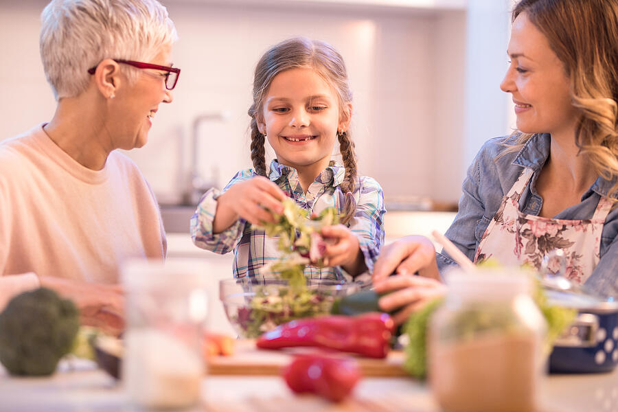 Happy girl making salad with her mother and grandmother. Photograph by Skynesher