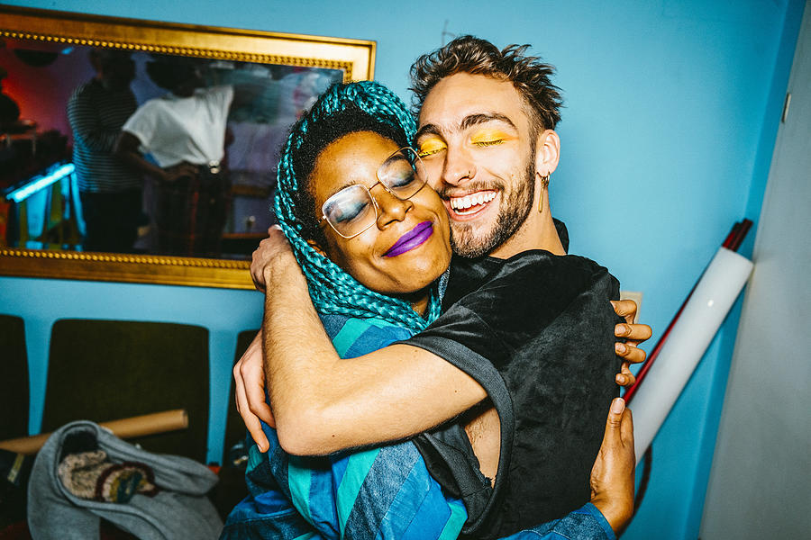 Happy male and female hipster friends hugging each other in living room Photograph by Maskot