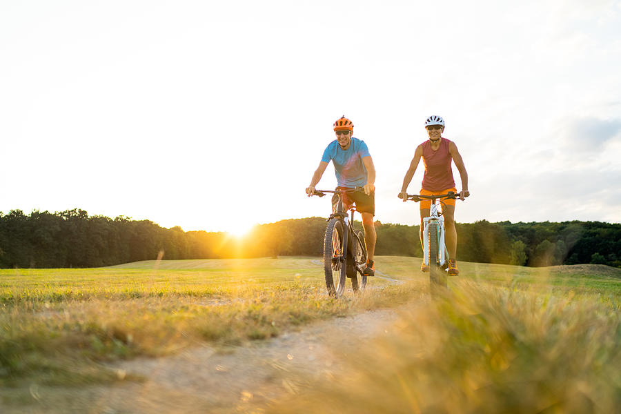 Happy Mature Adult Sporty Couple On Mountainbikes In Rural Landscape At Sunset Photograph by Amriphoto