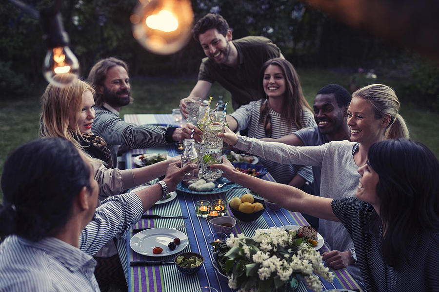 Happy multi-ethnic friends toasting drinks at dinner table in yard Photograph by Maskot