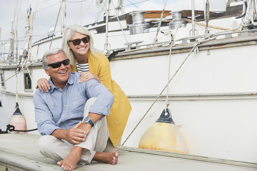 Happy senior couple sitting on boat dock Photograph by Kali9