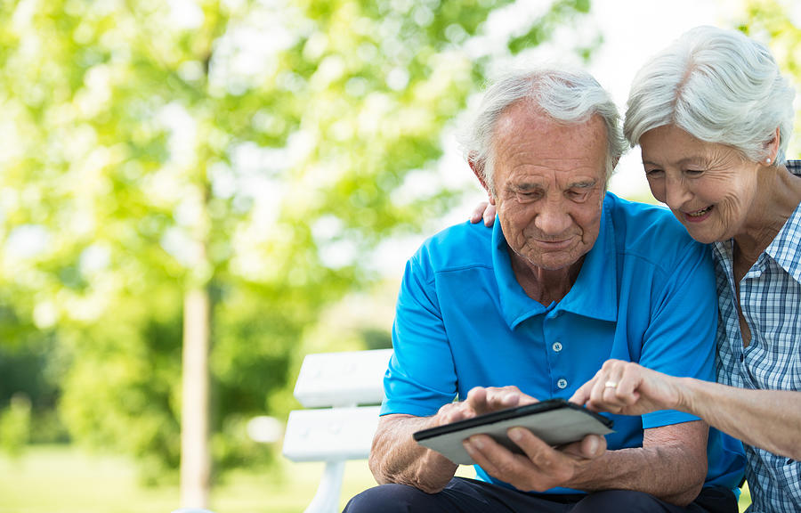 Happy senior couple using digital tablet in park. Photograph by Tashi-Delek