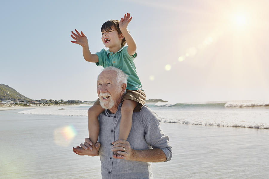 Happy senior man with grandson on his shoulders on the beach Photograph by Westend61
