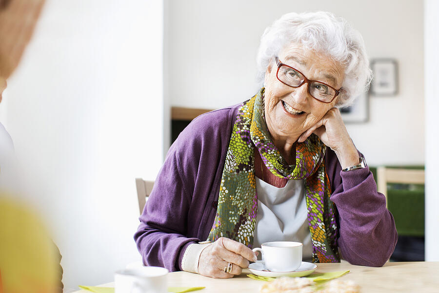 Happy senior woman looking at friend while having coffee at breakfast table in nursing home Photograph by Maskot