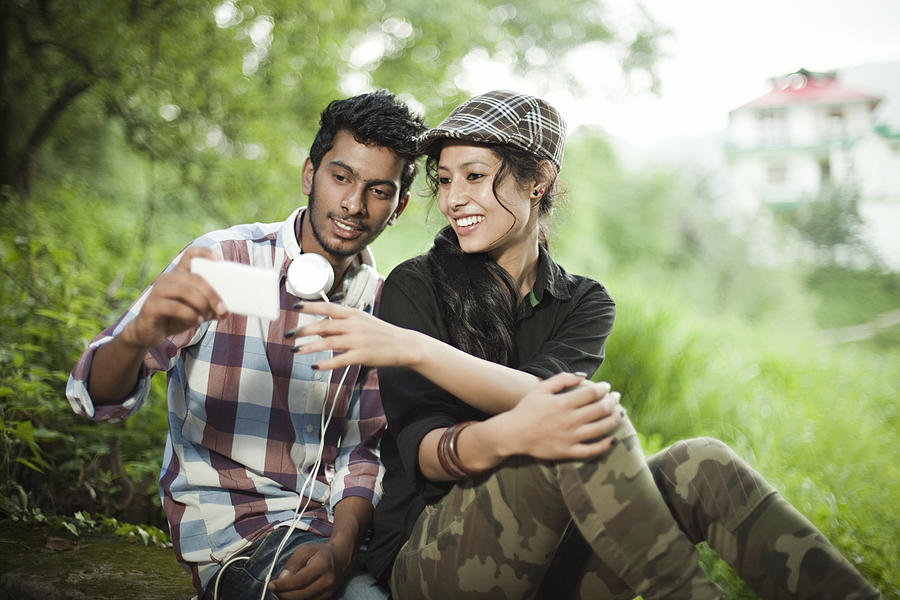 Happy teenage boy and girl of different ethnicity sharing smartphone. Photograph by Gawrav