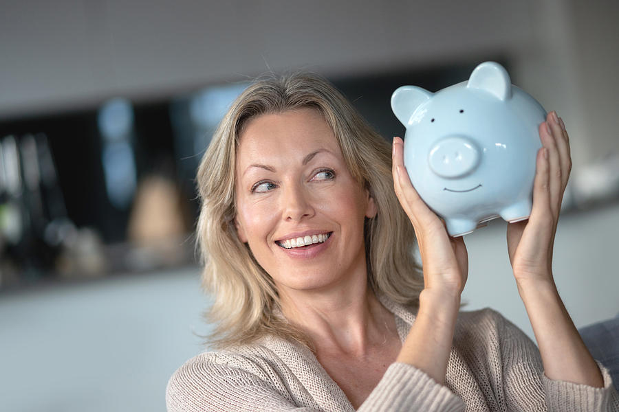 Happy woman at home holding a piggybank with her savings Photograph by Andresr