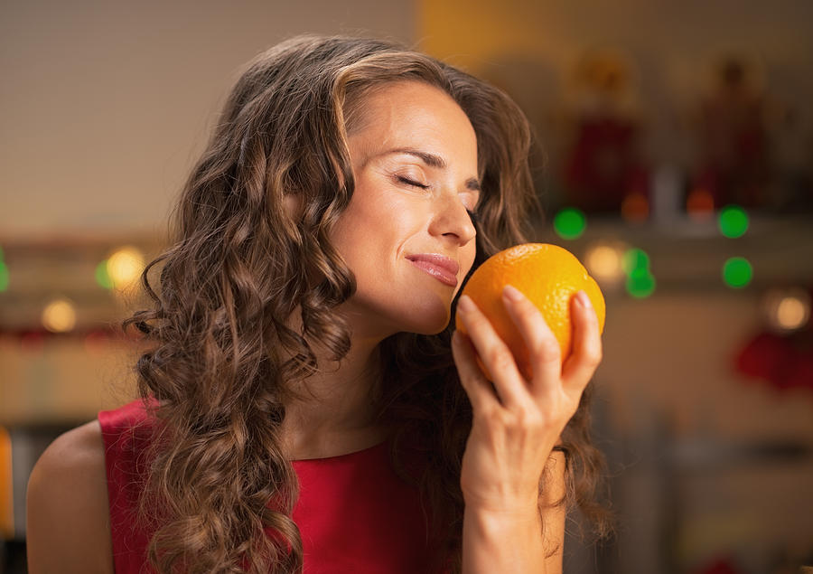 Happy woman enjoying orange in christmas decorated kitchen Photograph by CentralITAlliance